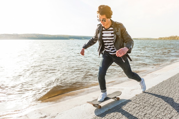 Giovane con uno skateboard vicino al mare