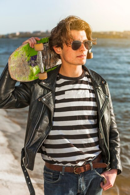海のそばのスケートボードを持つ若い男