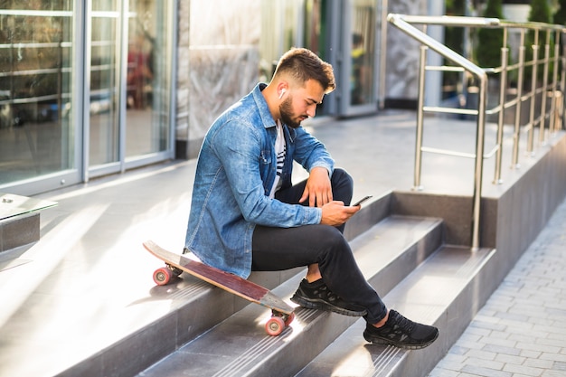 Young man with skateboard using mobile phone