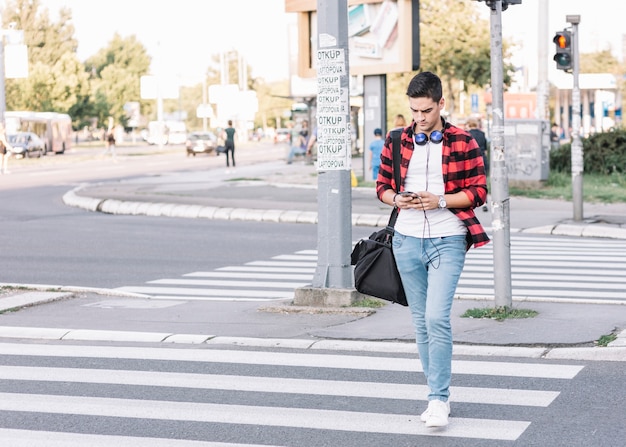 Young man with smartphone crossing street