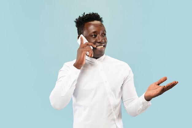 Young man with smartphone isolated on blue studio wall