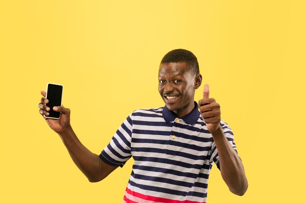 Young man with smartphone isolated on yellow studio wall