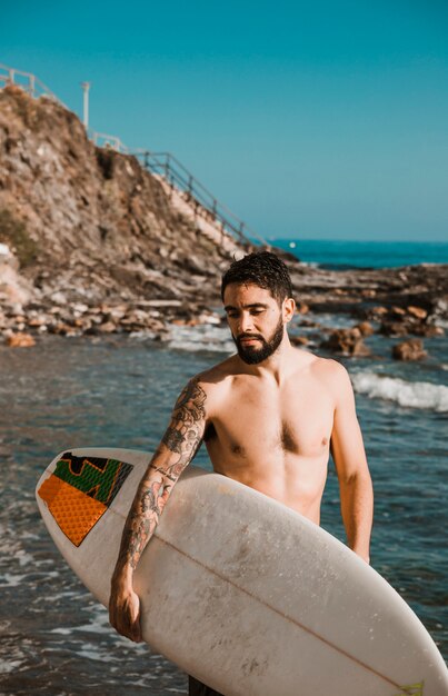 Young man with surf board on beach near water