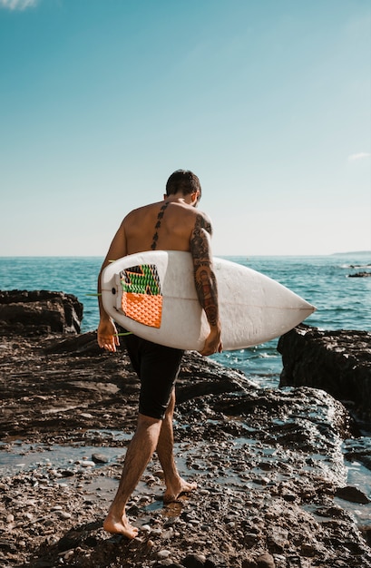 Бесплатное фото Молодой человек с доской для серфинга собирается на воду