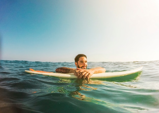 青い水の中でサーフボードを持つ若い男