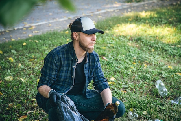 A young man with a trash bag in the forest cleans up plastic bottles