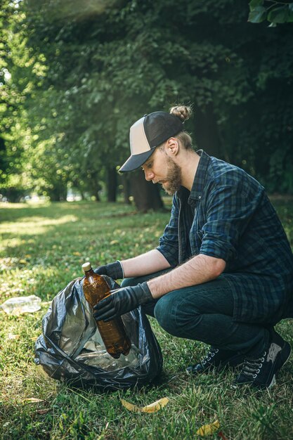 A young man with a trash bag in the forest cleans up plastic bottles