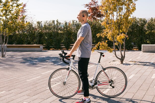 Молодой человек с беспроводной Bluetooth, стоя с белым велосипедом в парке