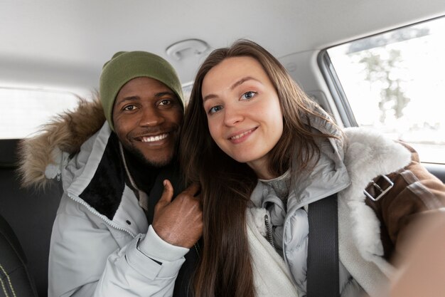 Young man and woman in the car taking selfie together before winter road trip