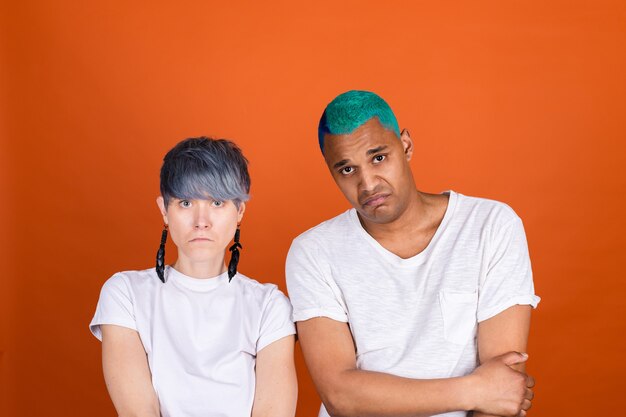 Young man and woman in casual white on orange wall look unhappy to camera