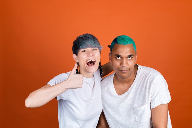 Young man and woman in casual white on orange wall woman with crazy emotions show thumb up man rolling eyes up