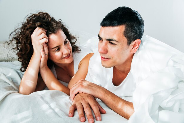 Young man and woman under duvet lying on bed 