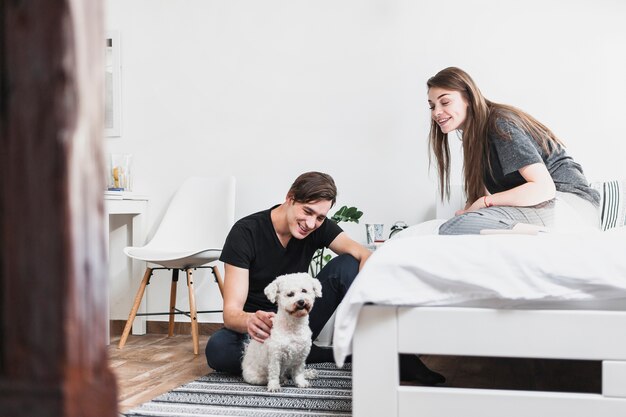 Young man and woman looking at their dog in bedroom