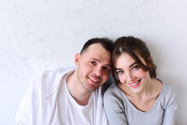 Young man and woman sit side by side in a white room