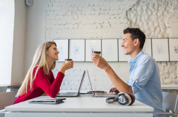 젊은 남자와 여자는 얼굴을 마주보고 테이블에 앉아 공동 작업 사무실에서 노트북에서 작업
