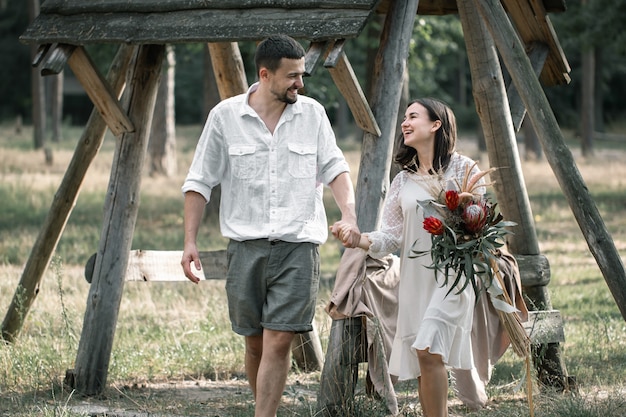 エキゾチックな花の花束を持ったおしゃれな服を着た若い男性と女性が、自然の中でデートしながら森の中を歩いています。