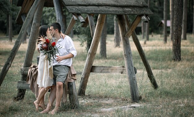 エキゾチックな花の花束で、森の中でキスをし、結婚のロマンスの概念で、スマートな服を着た若い男性と女性。