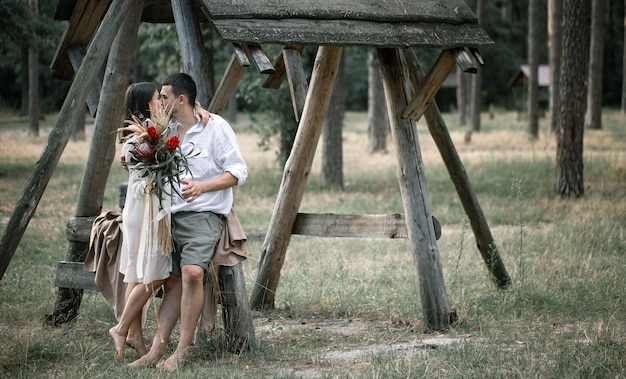 젊은 남자와 여자는 이국적인 꽃의 꽃다발과 함께 세련되게 옷을 입고, 숲에서 키스, 결혼에서의 로맨스의 개념.