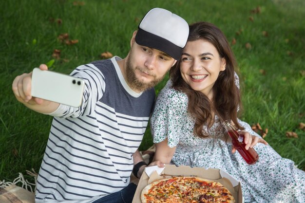 Молодой мужчина и женщина делают селфи с пиццей на пикнике