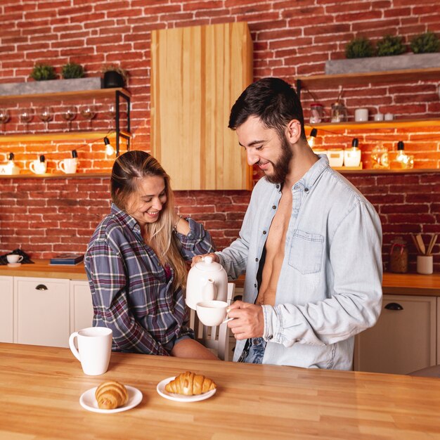 Young man and woman taking breakfast with tea and croissants