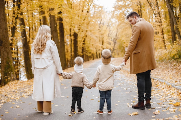 Young man, woman and their children walking outside wearing beige coats. Blond mother, brunette father, little girl and boy holding hands. Parents wearing coats, children - hats.