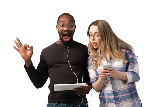 Young man and woman using laptop, devices, gadgets isolated on white  wall. Concept of modern technologies, tech, emotions, ad. Copyspace. Shopping, gaming, meeting online education.