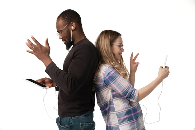 Free photo young man and woman using laptop, devices, gadgets isolated on white  wall. concept of modern technologies, tech, emotions, ad. copyspace. shopping, gaming, meeting online education.