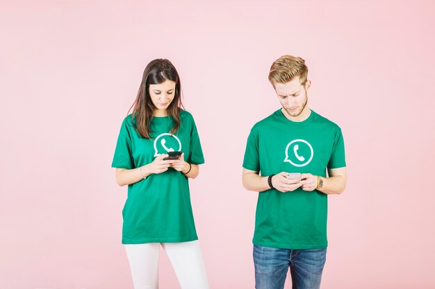 Young man and woman using mobile phone on pink background