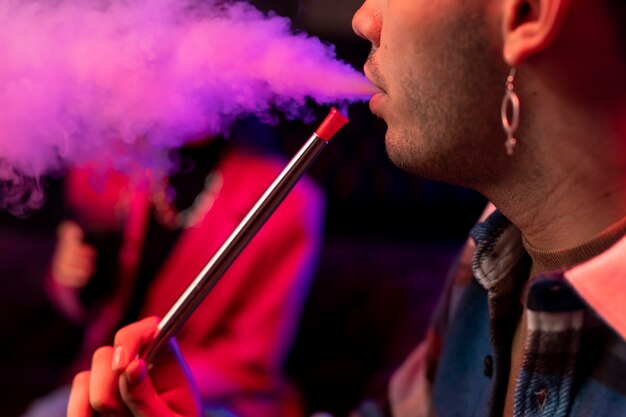 Young man and woman vaping from a hookah indoors