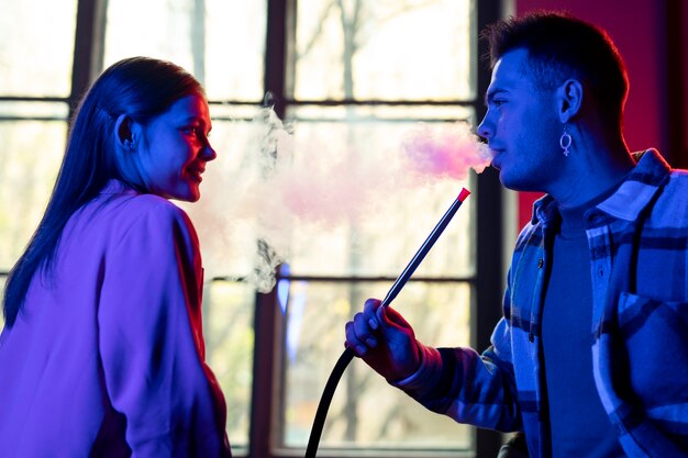 Young man and woman vaping from a hookah indoors