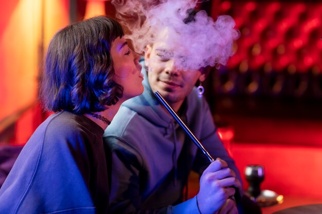 Young man and woman vaping from a hookah indoors