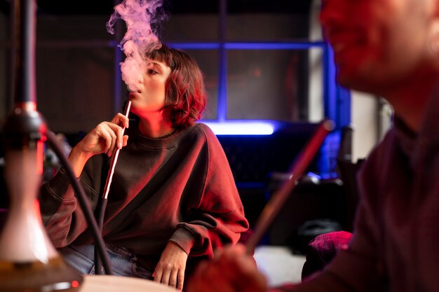 Young man and woman vaping from a hookah indoors