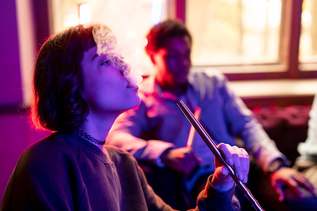 Young man and woman vaping from a hookah indoors