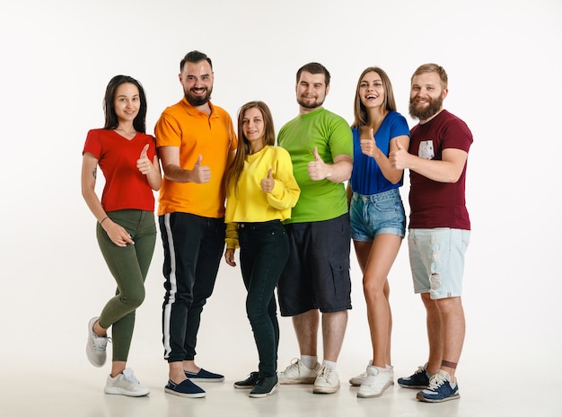 Молодой мужчина и женщина в цветах флага ЛГБТ на белой стене. Кавказские модели в ярких рубашках. Выглядите счастливым, улыбающимся и обнимающимся. Концепция гордости, прав человека и выбора ЛГБТ.