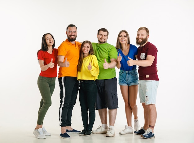 Молодой мужчина и женщина в цветах флага ЛГБТ на белой стене. Кавказские модели в ярких рубашках. Выглядите счастливым, улыбающимся и обнимающимся. Концепция гордости, прав человека и выбора ЛГБТ.
