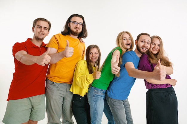 Young man and woman weared in LGBT flag colors on white wall. Caucasian models in bright shirts. Look happy together, smiling and hugging. LGBT pride, human rights and choice concept.