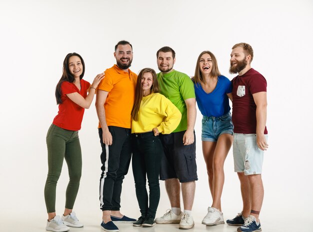 Young man and woman weared in LGBT flag colors on white wall. Caucasian models in bright shirts.