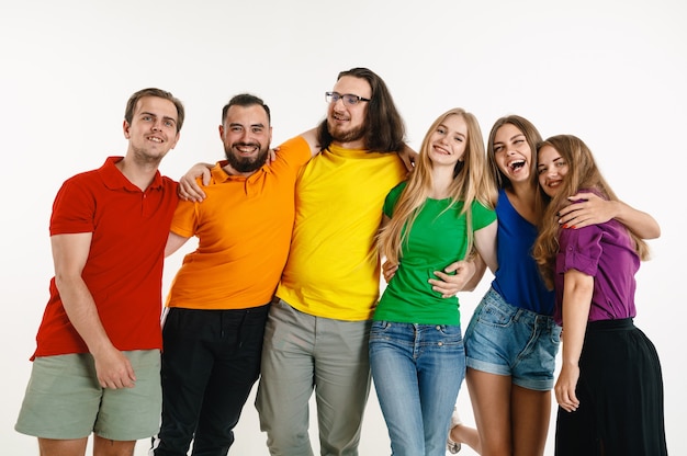 Young man and woman weared in LGBT flag colors on white wall. Caucasian models in bright shirts.