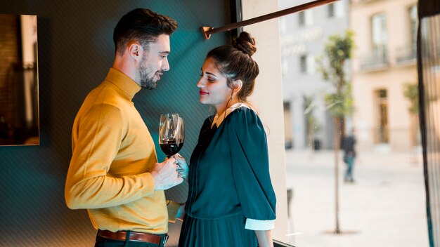 Young man and woman with glasses of wine near window 