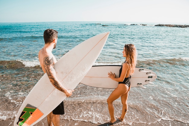 Giovane uomo e donna con tavole da surf sulla riva vicino all'acqua