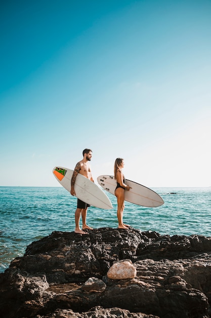 海の近くの石の上のサーフボードを持つ若い男女