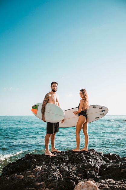 Молодой мужчина и женщина с досками для серфинга на камне возле воды