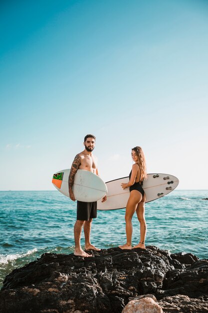 물 근처 돌에 서핑 보드와 함께 젊은 남자와 여자