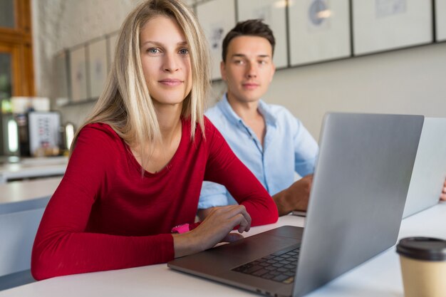 Young man and woman working on laptop in open space co-working office room,