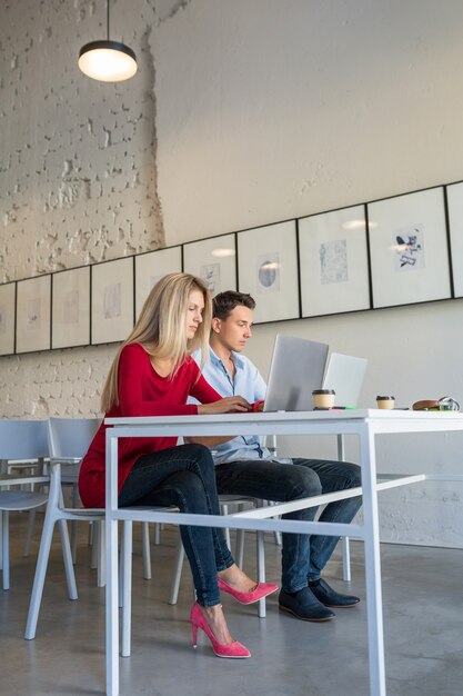 Young man and woman working on laptop in open space co-working office room,