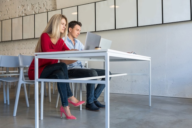 Young man and woman working on laptop in open space co-working office room