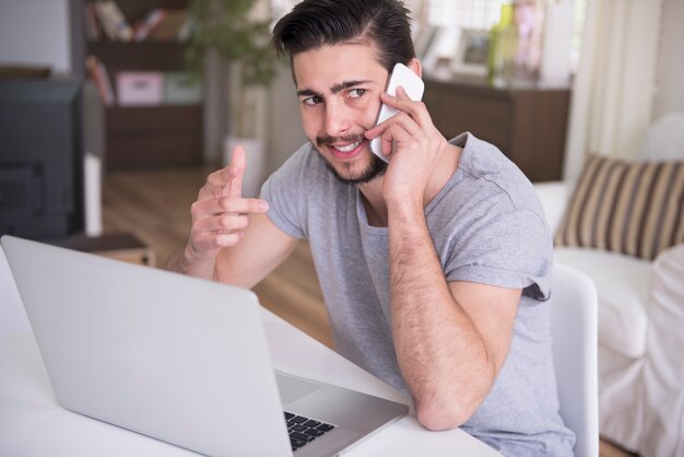 彼のラップトップで自宅で作業し、電話で話している若い男