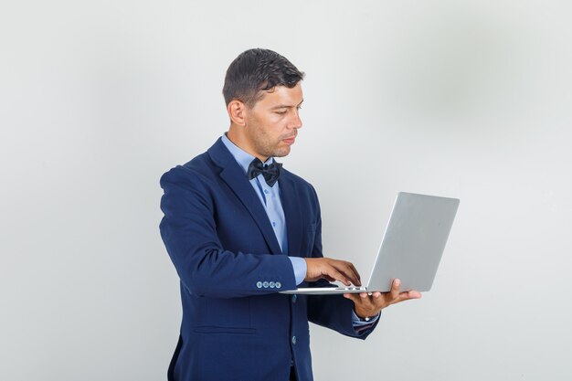 Молодой человек работает на ноутбуке в костюме и выглядит занятым.