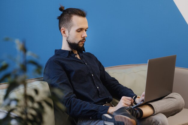 Young man working on the laptop while sitting on the sofa in the office