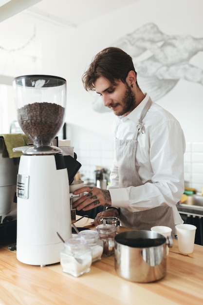 エプロンのレストランバリスタのバーカウンターでコーヒーマシンで働いている若い男とカフェのコーヒーマシンでコーヒーを作る白いシャツコーヒーショップでバリスタとして働いている少年